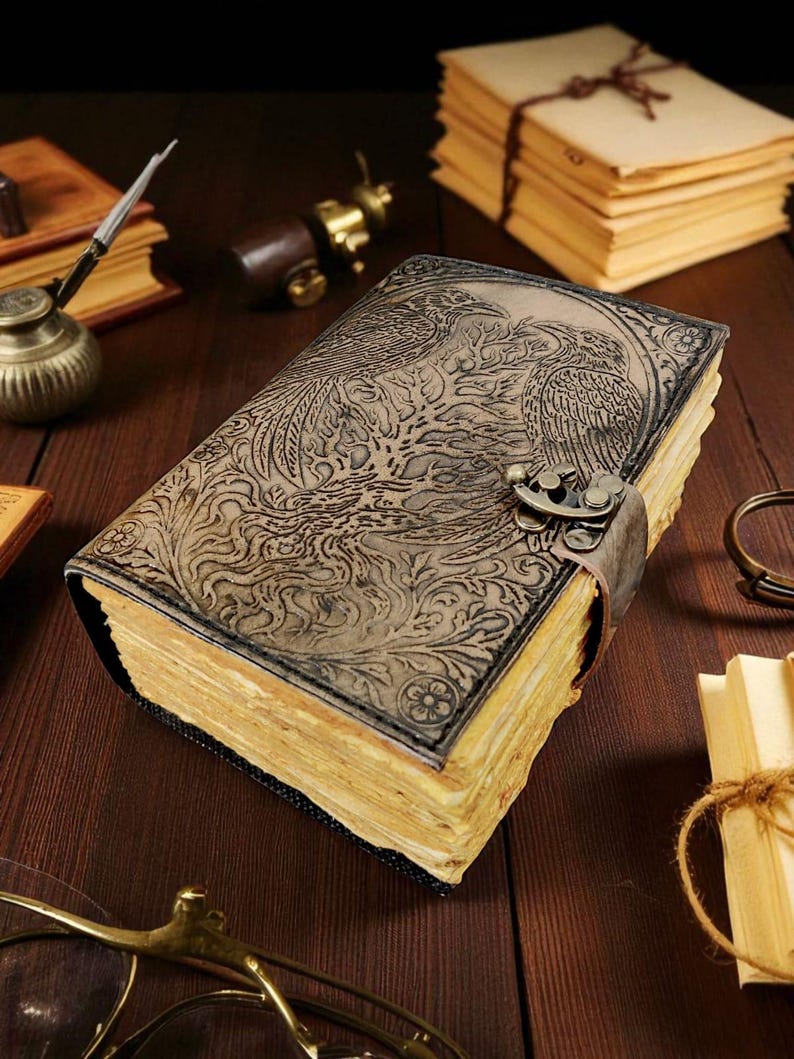 Puede incluir: Un diario encuadernado en cuero con un dise&ntilde;o de f&eacute;nix en relieve. El diario tiene un cierre de metal y una correa de cuero. Las p&aacute;ginas est&aacute;n envejecidas y la cubierta es de color marr&oacute;n oscuro. Sobre una superficie de madera.