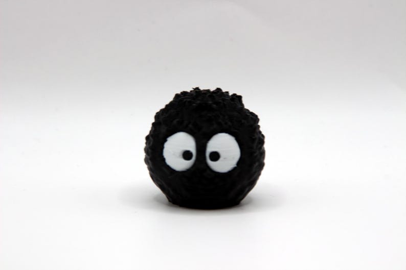 May include: A black fuzzy toy with two white eyes. The toy is round and has a textured surface.