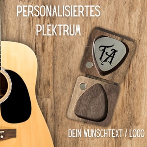 Könnte beinhalten: Eine Holzkiste mit einem Scharnierdeckel, die ein silbernes Plektrum mit den eingravierten Initialen "TA" enthält. Die Kiste steht auf einer Holzoberfläche neben einer Akustikgitarre. Der Text "PERSONALISIERTE PLEKTRUM" befindet sich über der Kiste, und der Text "DEIN WUNSCHTEXT / LOGO" befindet sich unter der Kiste.