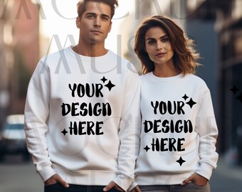 May include: Two people wearing white sweatshirts with the text "YOUR DESIGN HERE" in black. The sweatshirts have a crew neck design and are plain white. The text is accompanied by star graphics. The background is a blurred outdoor scene.