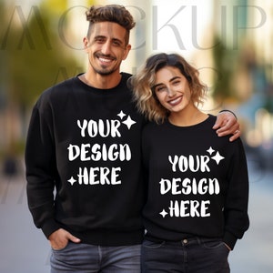 May include: Two black sweatshirts with the text "YOUR DESIGN HERE" in white. The sweatshirts are crew neck style. The image shows a man and a woman wearing the sweatshirts, smiling at the camera.