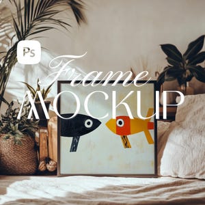 Può includere: Un'immagine incorniciata in nero con un dipinto astratto colorato di due pesci. L'immagine è su un letto bianco con un cuscino bianco e una pianta verde sullo sfondo.
