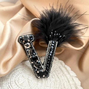 Peut inclure: Broche en forme de lettre V noire avec un accent en plume noire.