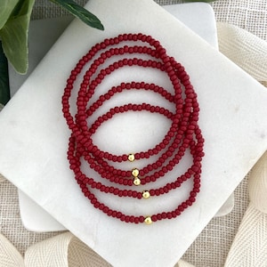 May include: Six red beaded bracelets with gold-colored accents. The bracelets are made of small, round beads and are arranged in a circular pattern. The gold accents are small, round beads that are spaced evenly around the bracelets.