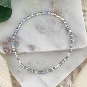 May include: A delicate beaded bracelet featuring alternating light blue and silver-colored beads. The bracelet is strung together, creating a flexible and stylish accessory. The beads are small and round, giving the bracelet a subtle, elegant appearance.