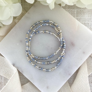 May include: A set of three circular bracelets composed of small, alternating matte light blue and metallic silver beads. The beads are strung together in a repeating pattern, creating a uniform and delicate appearance for each individual bracelet.