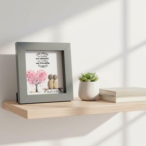 May include: A framed print with a gray border, featuring a heart-shaped pink tree and two pebble figures on a bench. The text reads "Our laughs are limitless, our memories are endless, our friendship is endless."