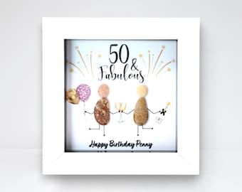 May include: A framed artwork with a white border. The artwork features two pebble figures celebrating a 50th birthday. The text reads "50 & Fabulous" and "Happy Birthday Penny". The figures hold balloons and champagne.