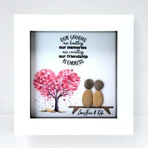 May include: A framed art piece with a white border. The artwork features a pink heart-shaped tree, two pebble figures on a bench, and the text "OUR LAUGHS are limitless, our memories are countless, our friendship IS ENDLESS".