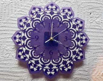 May include: Purple clock with a mandala design and white numbers. The clock face is a light purple with darker purple accents. The clock hands are white.
