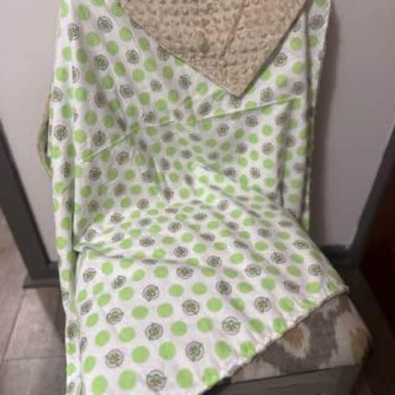 Puede incluir: Manta de beb&eacute; verde y blanca con un patr&oacute;n de lunares que presenta peque&ntilde;os c&iacute;rculos verdes con un contorno blanco. La manta est&aacute; hecha de tela suave y felpa y tiene un respaldo de vell&oacute;n beige.