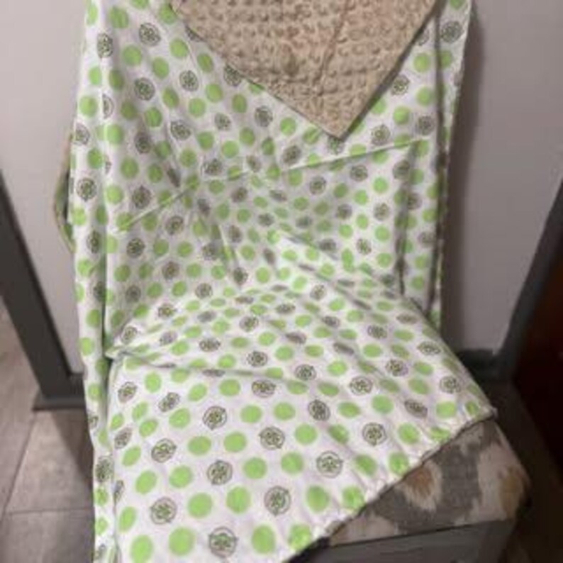 Puede incluir: Manta de beb&eacute; verde y blanca con un patr&oacute;n de lunares que presenta peque&ntilde;os c&iacute;rculos verdes con un contorno blanco. La manta est&aacute; hecha de tela suave y felpa y tiene un respaldo de vell&oacute;n beige.