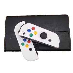 May include: White Nintendo Switch Joy-Con controllers with colourful buttons and a black analogue stick. The controllers are attached to a black Nintendo Switch console.