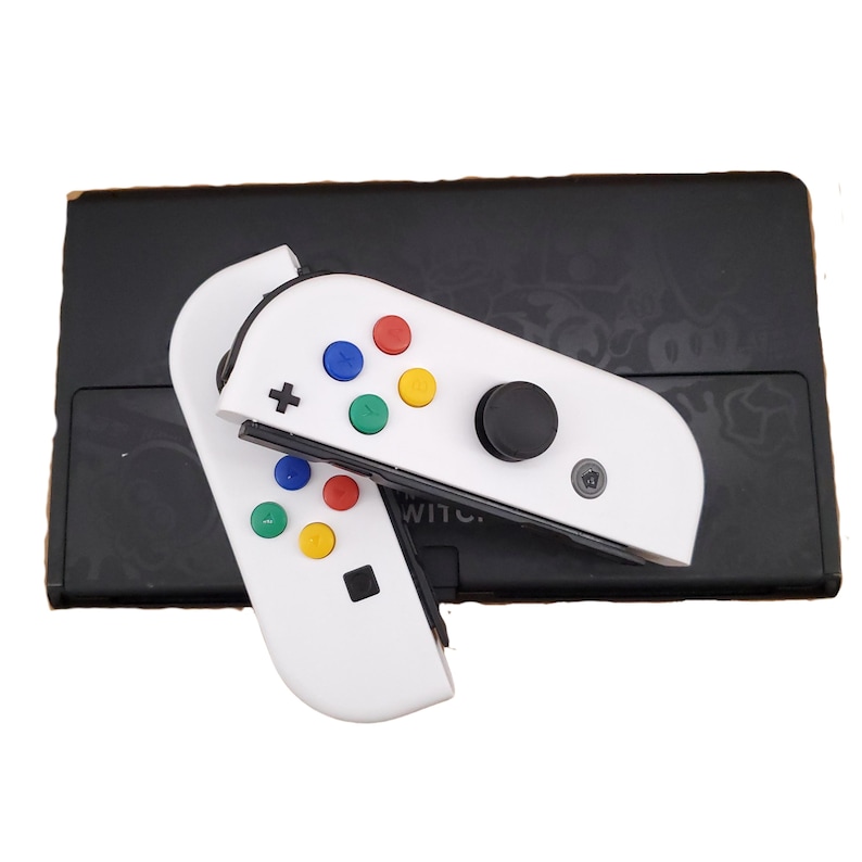 May include: White Nintendo Switch Joy-Con controllers with colourful buttons and a black analogue stick. The controllers are attached to a black Nintendo Switch console.
