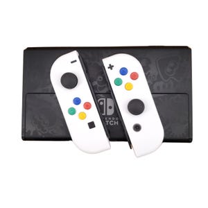 May include: A pair of white Nintendo Switch Joy-Con controllers with colourful buttons. The controllers are on top of a black Nintendo Switch console with a design of a squid.