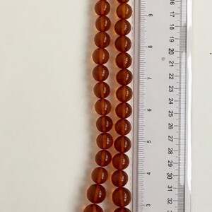 Puede incluir: Un collar de cuentas de &aacute;mbar, de aproximadamente 50 cm de largo, con una regla para la escala. Las cuentas son de un color &aacute;mbar oscuro y rico y tienen forma redonda.