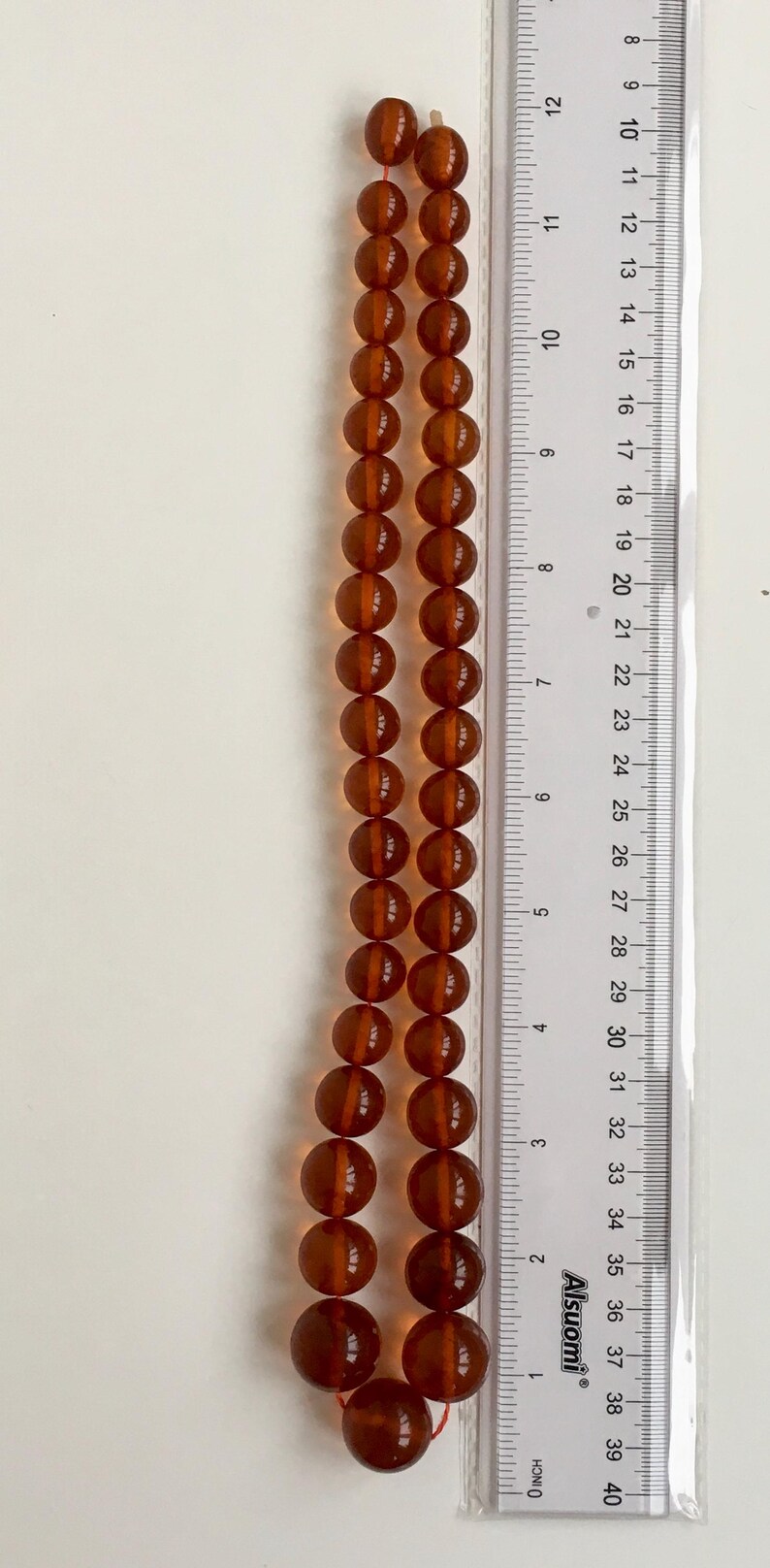 Puede incluir: Un collar de cuentas de &aacute;mbar, de aproximadamente 50 cm de largo, con una regla para la escala. Las cuentas son de un color &aacute;mbar oscuro y rico y tienen forma redonda.