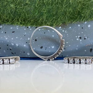 May include: A set of three silver rings with clear cubic zirconia stones. The rings are arranged on a gray speckled surface.