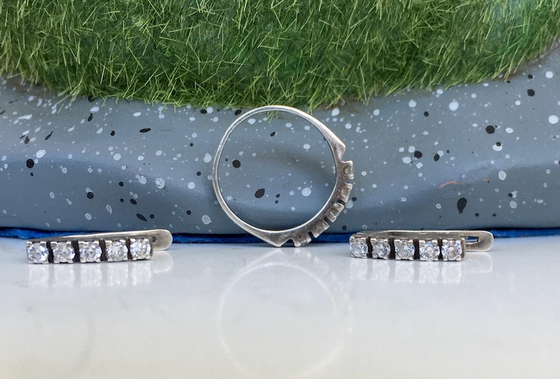 May include: A set of three silver rings with clear cubic zirconia stones. The rings are arranged on a gray speckled surface.