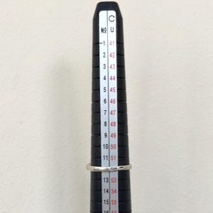 May include: A black ring sizer with white markings. The numbers on the sizer range from 41 to 57.