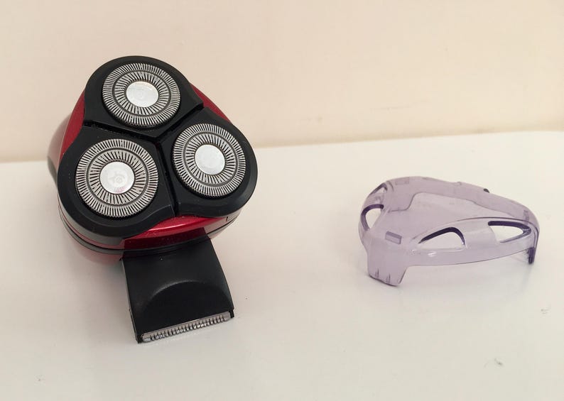 May include: A red electric razor with three rotating blades. The razor has a black handle and a clear plastic cover.
