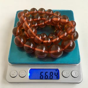 Puede incluir: Un collar de cuentas de &aacute;mbar en una b&aacute;scula digital, que pesa 66,84 gramos. Las cuentas son de un color marr&oacute;n c&aacute;lido y rico y tienen un acabado liso y pulido.
