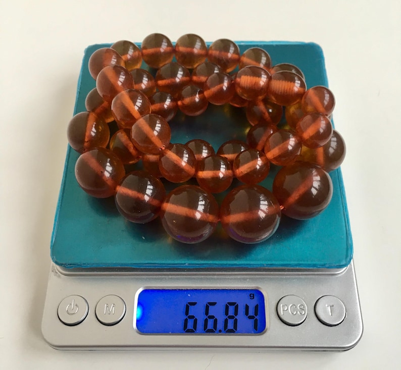 Puede incluir: Un collar de cuentas de &aacute;mbar en una b&aacute;scula digital, que pesa 66,84 gramos. Las cuentas son de un color marr&oacute;n c&aacute;lido y rico y tienen un acabado liso y pulido.