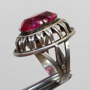 Pode incluir: Um anel de prata com uma grande gema rosa facetada engastada em um delicado design vazado.