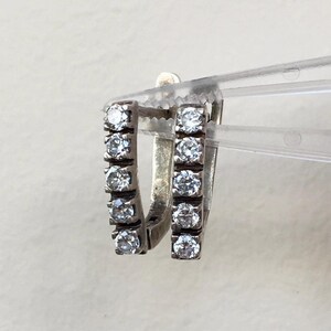 May include: A pair of silver hoop earrings with a row of clear cubic zirconia stones on each hoop.