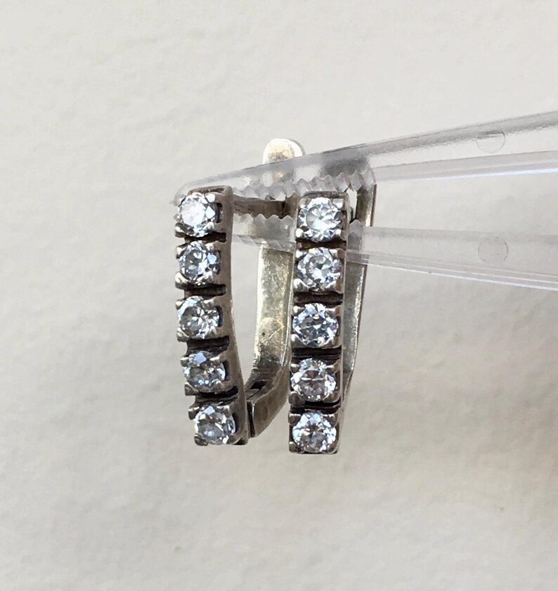 May include: A pair of silver hoop earrings with a row of clear cubic zirconia stones on each hoop.