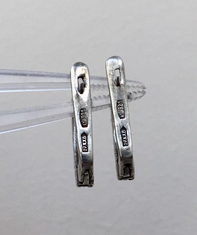 May include: A pair of silver hoop earrings with a hallmark that reads "925 585" and "7.7XB".