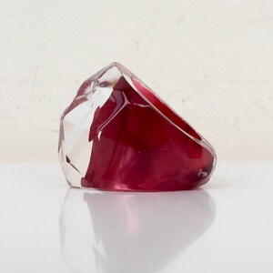 May include: A clear and red resin ring with a faceted design. The ring is made of two pieces of resin, one clear and one red, that are joined together.