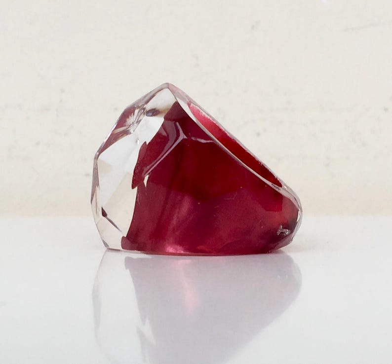 May include: A clear and red resin ring with a faceted design. The ring is made of two pieces of resin, one clear and one red, that are joined together.