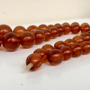 Puede incluir: Una larga hebra de cuentas de &aacute;mbar, con un c&aacute;lido color miel. Las cuentas son redondas y lisas, y el collar est&aacute; enhebrado en un cord&oacute;n fino y blanco.