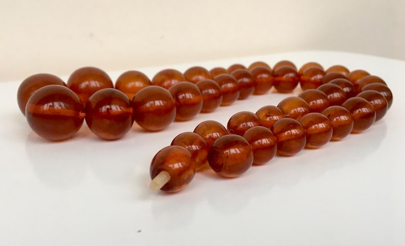 Puede incluir: Una larga hebra de cuentas de &aacute;mbar, con un c&aacute;lido color miel. Las cuentas son redondas y lisas, y el collar est&aacute; enhebrado en un cord&oacute;n fino y blanco.