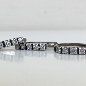 May include: A set of three silver rings with a row of clear cubic zirconia stones. The rings are all the same width and have a black enamel band on either side of the stones.