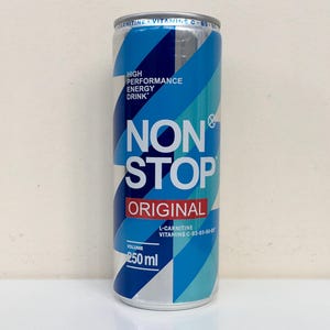 Puede incluir: Una lata de bebida energética de 250 ml con tapa y base plateadas. La lata presenta un diseño azul y blanco con las palabras "NON STOP ORIGINAL". Contiene "L-CARNITINA" y "VITAMINAS C-B3-B5-B6".