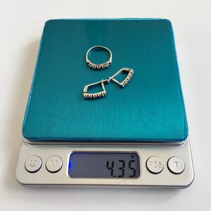 May include: A silver ring and earrings with small clear stones on a digital scale that reads 4.35 grams.
