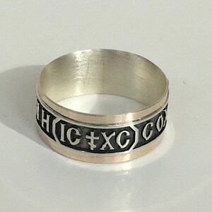 May include: A silver ring with a gold band and an inscription that reads "IC XC NIKA".