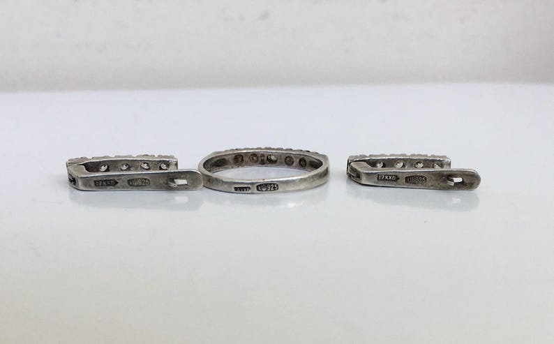 May include: A set of three silver rings with small clear stones set in the band. The rings are marked with the inscription "925" on the inside.