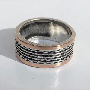 Puede incluir: Un anillo de plata con una banda de cobre y un diseño texturizado.