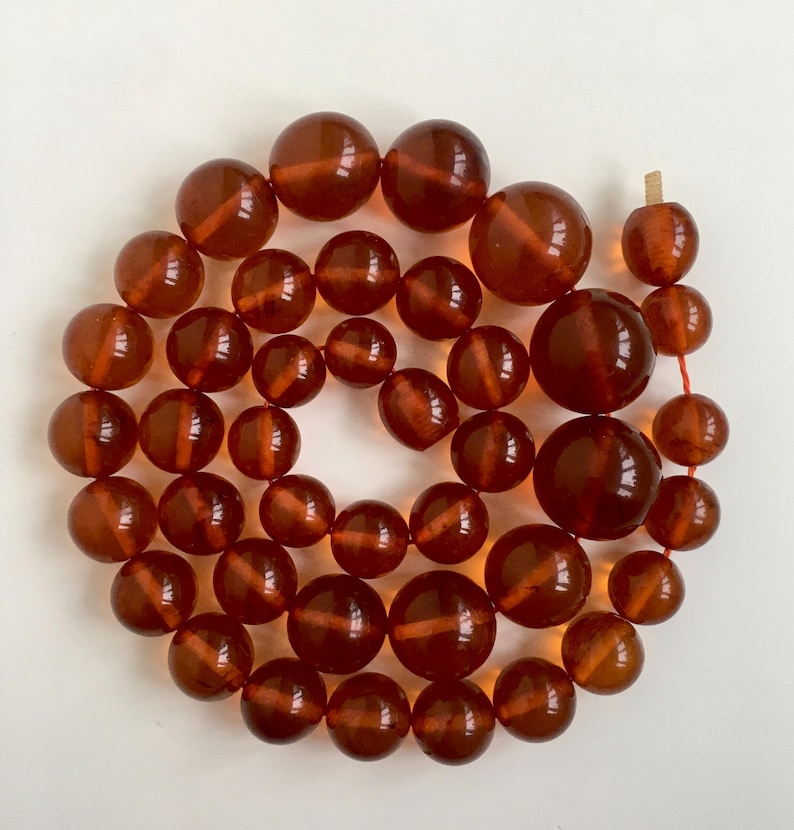 Puede incluir: Una larga hebra de cuentas de &aacute;mbar, cada cuenta es de un color marr&oacute;n intenso y rico y tiene un acabado liso y pulido. Las cuentas est&aacute;n enhebradas en un hilo rojo fino.