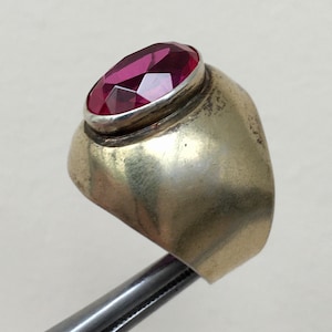 May include: A silver ring with a large, oval-shaped, faceted, dark pink gemstone.