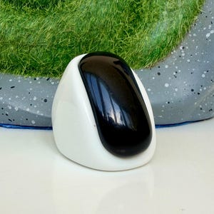 May include: A smooth, rounded object featuring a glossy black, elongated oval centre piece set within a solid white, curved frame. The object has a polished finish and a distinct contrast between the dark central element and the bright white border.