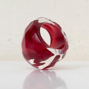 May include: A red and clear geometric ring with a faceted design. The ring is made of resin and has a unique, modern look.
