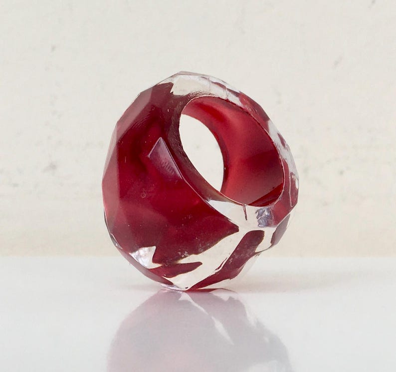 May include: A red and clear geometric ring with a faceted design. The ring is made of resin and has a unique, modern look.