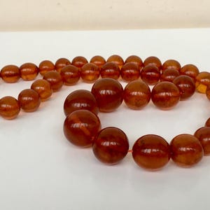 Puede incluir: Un collar largo de &aacute;mbar con cuentas grandes y redondas. Las cuentas son de un color marr&oacute;n c&aacute;lido y rico y tienen un acabado liso y pulido.