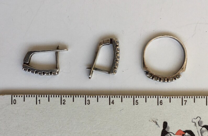 May include: Three silver rings with a decorative pattern. The rings are on a white surface with a ruler for scale.