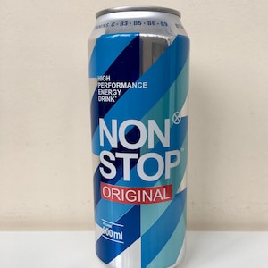 Puede incluir: Una lata de bebida energética plateada y azul con las palabras "NON STOP ORIGINAL" en blanco. La lata tiene un diseño geométrico y el texto "HIGH PERFORMANCE ENERGY DRINK". La lata contiene 500 ml.