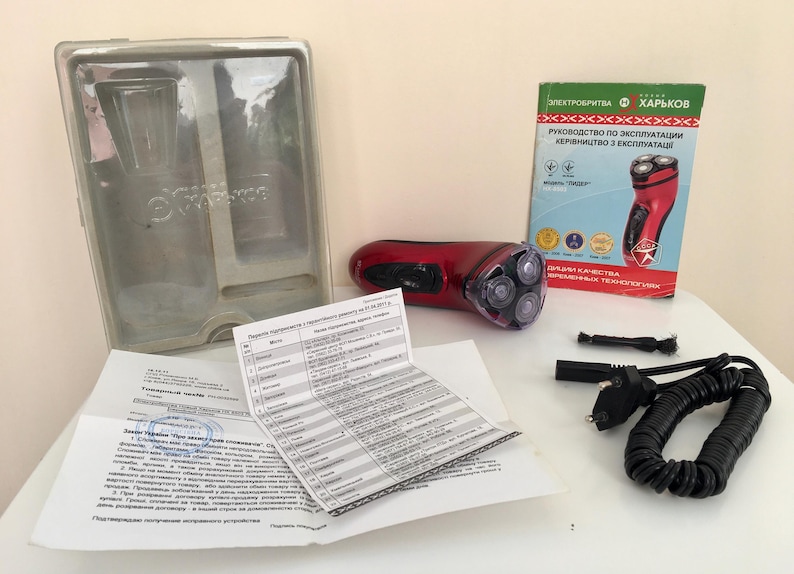 May include: A red electric shaver with a rotating head and a black cord. The shaver is packaged in a clear plastic box with instructions and a warranty card. The instructions are in Ukrainian and Russian.